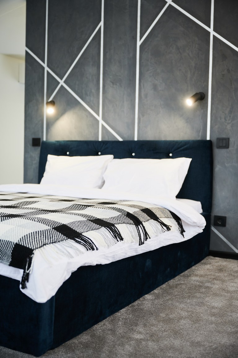 A navy velvet channel-tufted headboard anchors a large bed against a dark geometric-paneled accent wall.