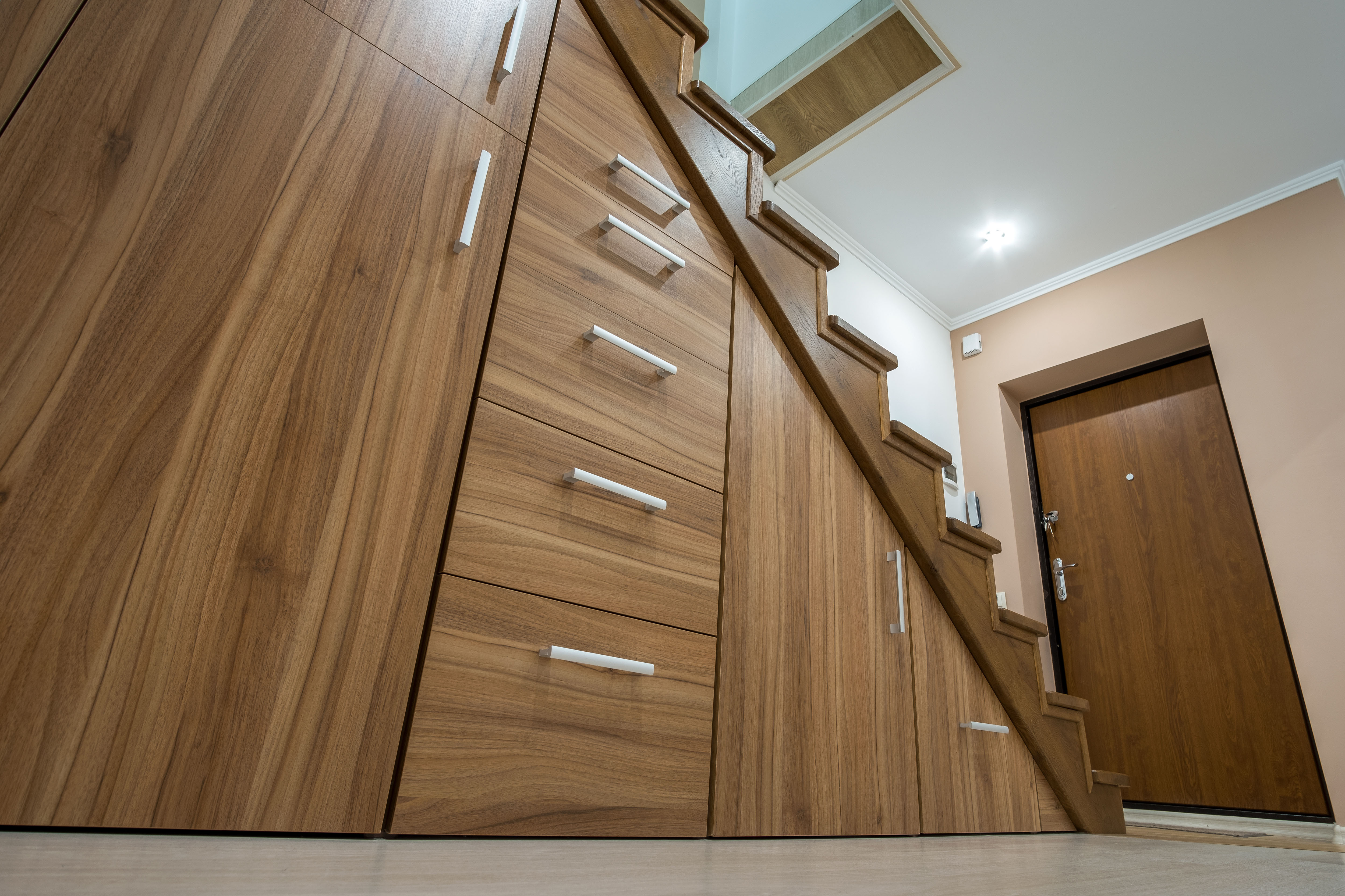 Built-in walnut cabinetry with a row of drawers is tucked beneath a staircase, its brushed metal pulls lined up beside the glass stair railing.