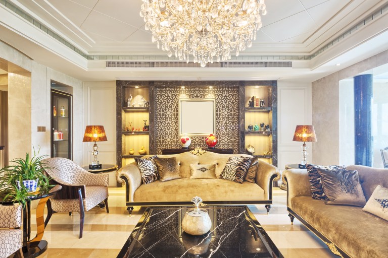 A gold-and-plum living room with a black marble coffee table, tufted sofas, and richly patterned drapery framing an arched doorway beneath a crystal chandelier.