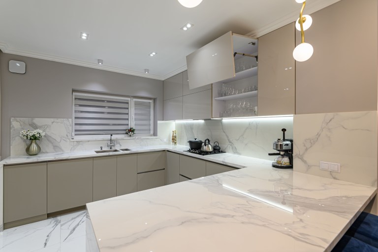 A veined white marble kitchen counter runs beneath pendant lights, with an espresso machine and coffee station set along the backsplash.