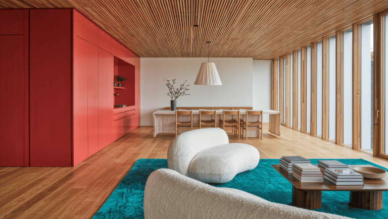 One large open room split into a living zone on a teal rug and a dining zone under a lowered slatted ceiling panel.