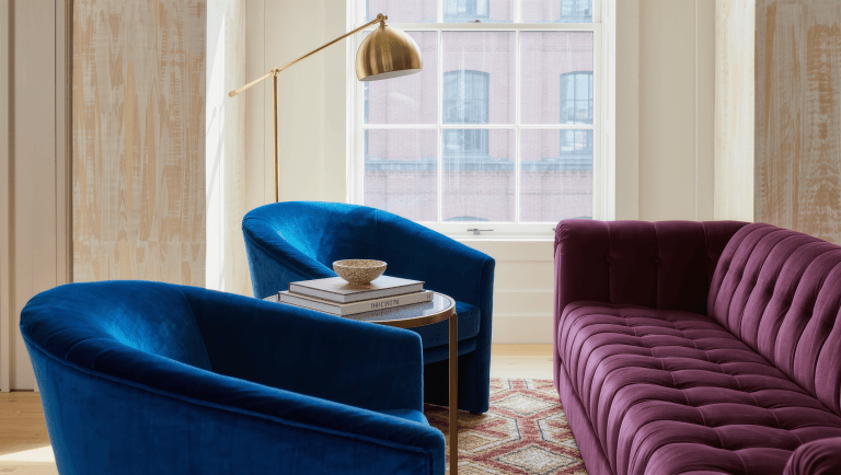 Two curved velvet armchairs angle toward a tufted sofa around a brass and marble side table, forming a conversation group.