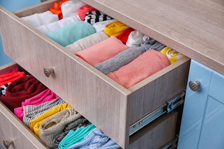 An open warm-wood drawer reveals neatly folded stacks of colorful clothing organized in tidy rows.