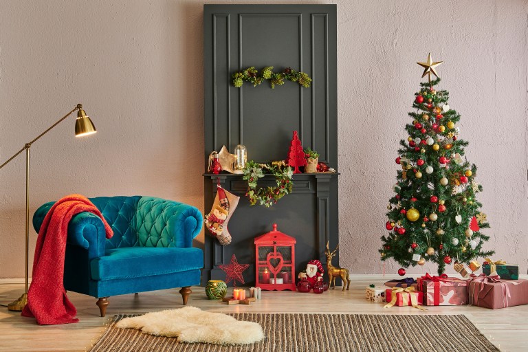 A compact holiday corner with a sapphire velvet chesterfield sofa, brass floor lamp, a decorated fir tree, and a garland draped above a dark painted doorway, leaving the floor clear.