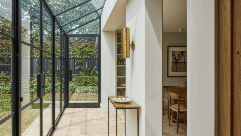 A slim brass console just outside the back door holds a stack of plates and folded linens, a landing surface for carrying food outdoors.